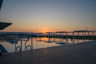 Güneş durgun suların ardında batarken, alacakaranlığın ılık renkleri gökyüzünü aydınlatıyor ve sakin bir atmosfer yaratıyor..