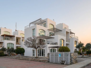 Geniş pencereli çağdaş binalar alacakaranlığın yumuşak parıltısında güneşleniyorlar, sakin bahçeler ve patikalarla çevrili..