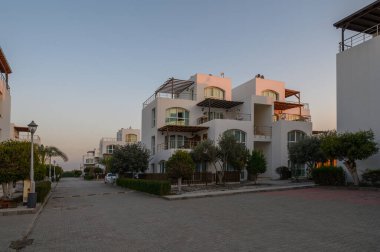 Şık beyaz binalar, batan güneşin altın ışığıyla yıkanmış sessiz bir yerleşim bölgesinde dururlar..