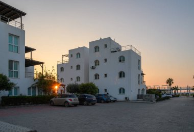 Sıcak güneş ışığı, sakin sahil şeridi yakınlarında gündüzleri geceye geçerken modern mimariyi yansıtıyor..