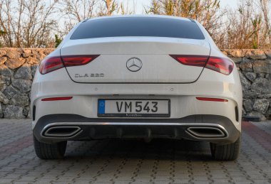 Gaziveren Kıbrıs Rum Kesimi - 30.01.2025 Batan güneşin sıcacık parıltısıyla parlayan taştan bir duvarın yanında duran ve kıvrımlarını gösteren parlak bir araç.