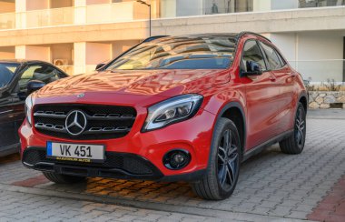 Gaziveren Kıbrıs Rum Kesimi - 30.01.2025 Canlı kırmızı bir SUV güneşli bir günde çağdaş binaların yakınındaki şablonlu kaldırımda dinleniyor.