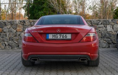 Gaziveren Kıbrıs Rum Kesimi -30.01.2025 Kırmızı bir spor araba alacakaranlıkta kırsal taştan bir duvara parlıyor, zarif kıvrımlarını vurguluyor.