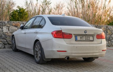Gaziveren Kıbrıs Rum Kesimi - 30.01.2025 İyi kullanılmış bir araba, yemyeşil bitkilerle çevrili ve yumuşak akşam ışığında yıkanmış sağlam bir taş duvarın yanında dinleniyor.