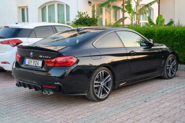 Gaziveren Kıbrıs Rum Kesimi -30.01.2025 Şık siyah spor coupe garaj yolunda dinleniyor, yeşil ışık yakınlarındaki sıcak akşam ışığı altında kıvrımlar ve zarafet sergiliyor.