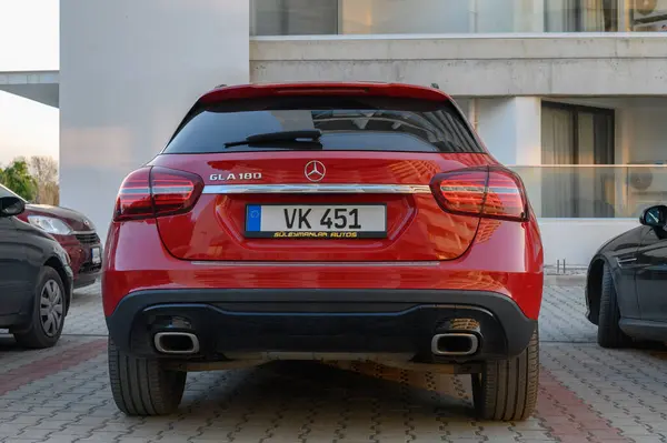 Gaziveren Kıbrıs Rum Kesimi - 30.01.2025 Altın güneş ışığı sıcak bir parıltı saçarken çağdaş binaların yakınında şık kırmızı bir SUV duruyor.