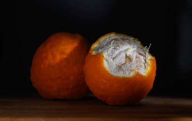 İki parlak turuncu meyve ahşap bir yüzeyde oturuyor, lifli dokuya sahip eşsiz beyaz bir iç mekan ortaya çıkarıyor..