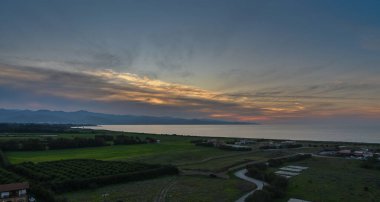Akşam çöktüğünde altın ışınlar yavaşça solar, sakin kıyı şeridini aydınlatır ve çevreleyen yeşil manzaraları aydınlatır.