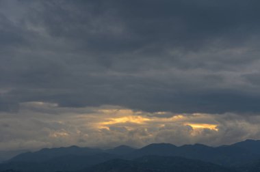 Karanlık, girdap gibi dönen bulutlar alacakaranlıkta görkemli dağları sarıyor. Yumuşak altın ışığın kısa görüntülerini ortaya çıkarıyor..