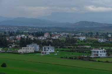 Çağdaş evlerle benekli gür tarım arazilerinin üzerinde yağmur bulutları beliriyor, dingin bir güzellik ortamı yaratıyor..