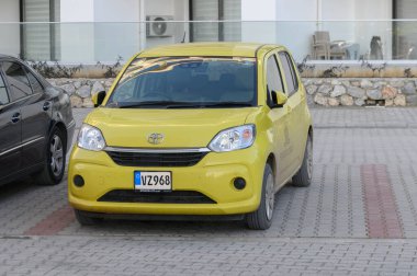 Gaziveren Kıbrıs Rum Kesimi - 03.02.2025 Canlı sarı renkli kompakt bir araba güneşli bir park yerinde, parlak siyah bir aracın yanında, kentsel yaşamı gözler önüne seriyor..