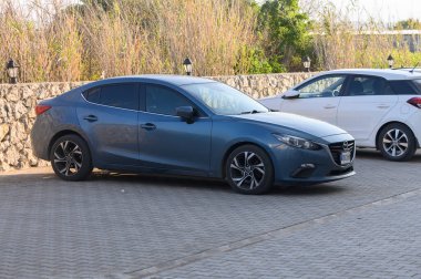 Gaziveren Kıbrıs Rum Kesimi - 03.02.2025 Şık mavi bir sedan, alacakaranlıkta yemyeşil ve taşların arasında huzur içinde dinleniyor..