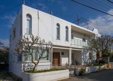 Güzel tasarlanmış, canlı bitkiler ve ağaçlarla çevrili, sakin bir günde güneşin altında güneşlenen beyaz bir ev..