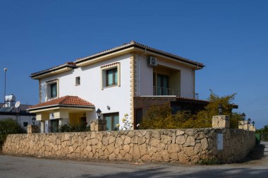 Fayanslı çatısı olan iki katlı güzel bir ev, canlı bir bitki örtüsü tarafından çerçevelenmiş, berrak mavi gökyüzüne gururla karşı duruyor..