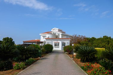 Canlı yeşillikler ve çiçek açan çiçeklerle çevrili güzel beyaz villa sıcak öğleden sonra güneşinin tadını çıkarıyor..