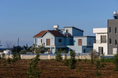 Büyüleyici mavi bir villa yeni dikilmiş ağaçların arasında oturuyor, kırsal kesimde güneşli bir sabahın sıcaklığında güneşleniyor..