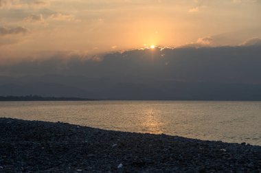 Bulutların arasından altın ışınlar çıkıyor, sakin suları aydınlatıyor ve sakin bir akşamda kayalık kıyıları aydınlatıyor..