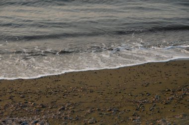 Karanlık çöktüğünde, yumuşak dalgalar taşlı bir sahile yuvarlanır ve suyun kenarında sakin bir atmosfer oluşturur..