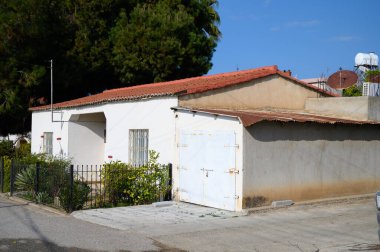 Kırmızı kiremit çatılı büyüleyici bir ev asfalt bir yolun yanında, açık mavi gökyüzünün altında yeşilliklerle çevrili..