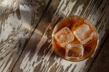 Buz küplü altın sıvı, sıcak ışıkla aydınlatılmış yıpranmış ahşabın üzerinde oturur. Sıcak, davetkar bir atmosfer yaratır..