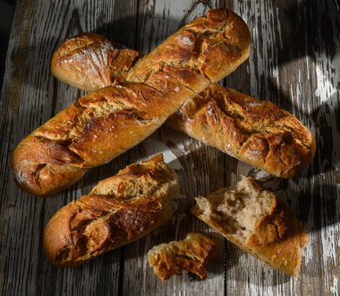 Golden crusted loaves of artisan bread sit on a weathered wooden surface, highlighting their texture and warmth. clipart