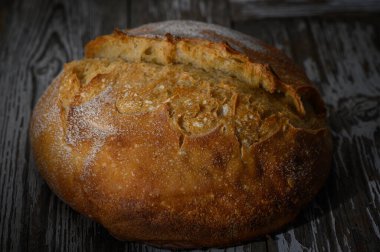 Taze pişmiş, altın kabuklu bir zanaatkar ekmeği, eskimiş ahşap bir masada dinleniyor, sıcaklık ve konfor yayıyor..