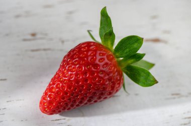 Olgun, canlı bir çilek eskimiş ahşap bir masada uzanır, taze ürünün ve doğal güzelliğin özünü yakalar..