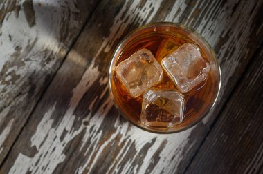 Üç buz küplü bir bardak koyu bir içecek, ahşap bir yüzeyde oturup rahatlamaya davetiye çıkarır..