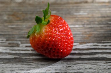 Lezzetli bir çilek, parlak kırmızı tonunu ve yumuşak ışığın altındaki küçük tohumları vurgulayan, eski ahşap bir masanın üzerinde uzanıyor..