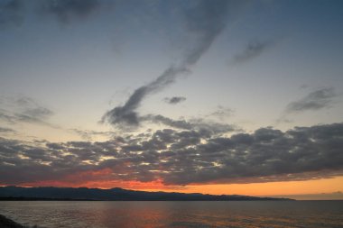 Güneş sakin suların üzerinde batarken altın ve kırmızı renkler gökyüzünde harmanlanarak sakin bir akşam atmosferi yaratır..