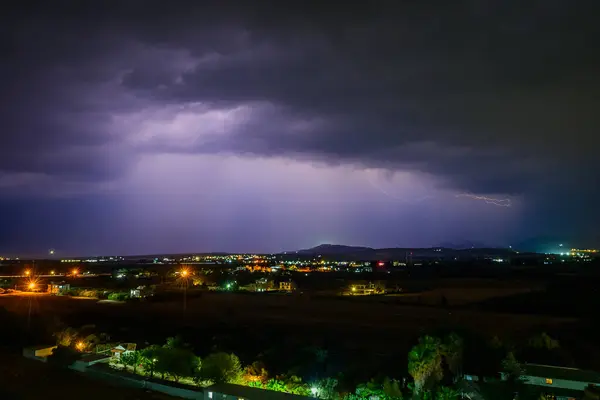 Parlak yıldırımlar sakin bir kasabanın üzerindeki kara bulutları delip geçer ve dramatik bir gece atmosferi yaratır..
