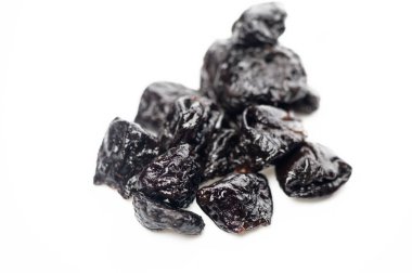 Koyu, buruşuk kuru erikler temiz, beyaz bir zemin üzerinde uzanır, zengin renklerini ve davetkar dokusunu sergilerler..