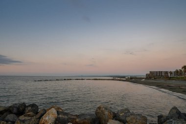 Yumuşak pastel gökyüzü sakin suları kucaklıyor alacakaranlık dingin sahil boyunca geceye dönüşürken.