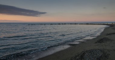 Yumuşak dalgalar kumlu sahili öperken ufuk huzurlu bir alacakaranlık anında ılık renklerle parlarken.