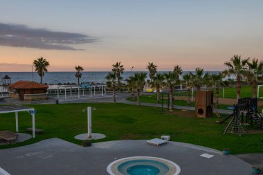 Sallanan palmiye ağaçları ve arka planda çarpıcı bir okyanus günbatımının yer aldığı sakin bir alacakaranlık kıyı parkını kucaklıyor..