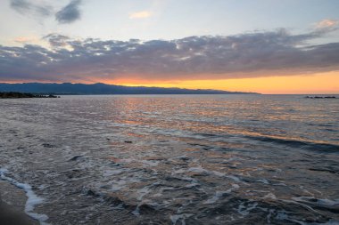 Güneş uzak dağların ardında batarken dalgalar yavaşça kıyıya vurur, gökyüzünü ılık renklerle boyarlar..