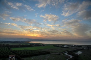 Güneşin battığı ufkun nefes kesen manzarası. Sahil kenarındaki huzurlu bir araziye sıcak renkler döküyor..
