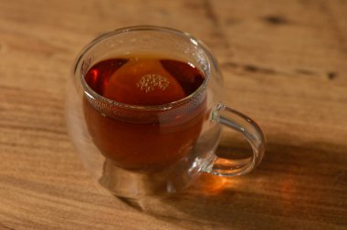 Dumanı tüten bir fincan çay, huzurlu bir öğleden sonra dokulu ahşap bir yüzeyde dinlenirken sıcaklık yayar..