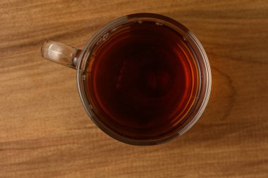 Dumanı tüten bir fincan siyah çay, kırsal bir ahşap yüzeyde oturur ve öğleden sonra ışığı altında sükunet hissi yayar..