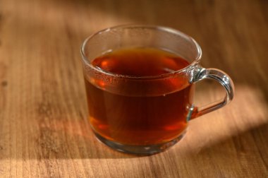 Berrak bir bardak kehribar çayı, yıpranmış ahşap bir yüzeye dayanır. Huzur ve rahatlık hissi yayar..