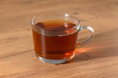 Temiz bir bardak kehribar çayı içerir. Yumuşak, ılık bir ışığın altında, ahşap bir masanın üstünde rahatlatıcı bir etki yaratır..