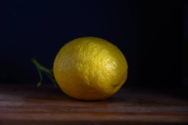 Canlı bir limon, ahşap bir yüzeyde tek başına oturur. Yumuşak ışıkla aydınlanır. Bu da onun dokusunu ve rengini arttırır..