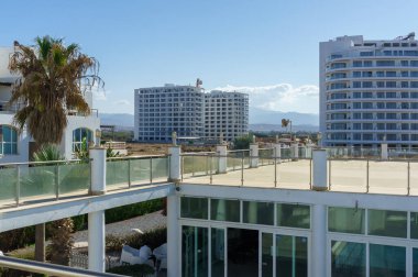 Parlak güneş ışığı çağdaş binaları ve bereketli palmiye ağaçlarını güçlendirir ve sakin bir kıyı atmosferi yaratır..