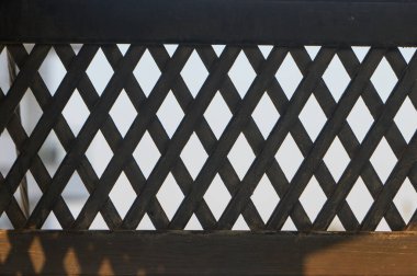 Ahşap bir kafes, güneş ışığında büyüleyici gölgeler bırakır. Karmaşık işçiliğini sergiler..