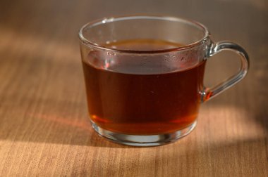 Konforlu bir ortamda, hafif güneş ışığıyla aydınlatılmış, bol bitkisel çayla dolu berrak bir fincan sergilenir..