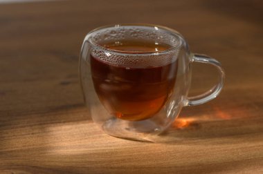 Bitki çayı berrak bir fincanda nazikçe buharlaşır, sıcak bir öğleden sonra güneşinde yıkanmış ahşap bir masada oturur..