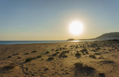 Nefes kesen bir gün batımı kumlu sahilde sıcak bir ışık yayar. Dalgalar yavaşça içeri girerken huzurlu bir atmosfer yaratır..
