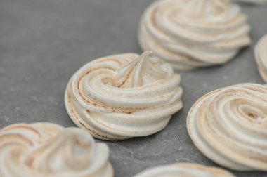Kremalar sanatsal olarak düzenlenmiştir, yumuşak kahverengi ve beyaz kıvrımları sergilenir pürüzsüz gri bir zemin üzerinde.