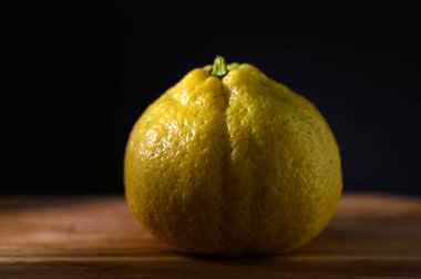 Ayırt edici sarı turunçgil meyvesi yumuşak ışıkla aydınlatılmış kırsal ahşap bir tahtanın üzerinde zarif bir şekilde duruyor..