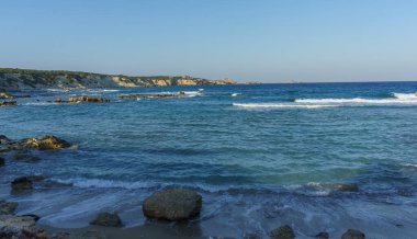 Güneş, dalgaların yavaşça kayalara ve kayalıklara çarptığı huzurlu bir kıyı şeridinde batar..